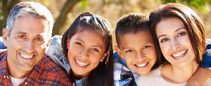 The image shows a family of four, including two adults and two children, posing for a photo with smiles on their faces.