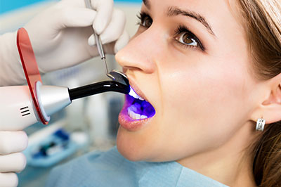 Woman receiving dental care with a specialized device, surrounded by medical equipment and professionals.