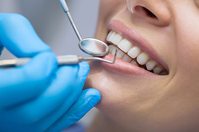 The image shows a person receiving dental care with a toothbrush in their mouth, and there is a dental hygienist wearing blue gloves and holding a mirror to inspect the teeth.