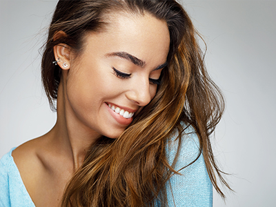 A smiling woman with long hair, looking down, against a neutral background.